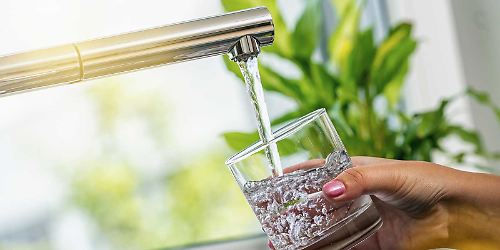 Frau-füllt-sich-Leitungswasser-am-Wasserhahn-in-ein-Glas-ab